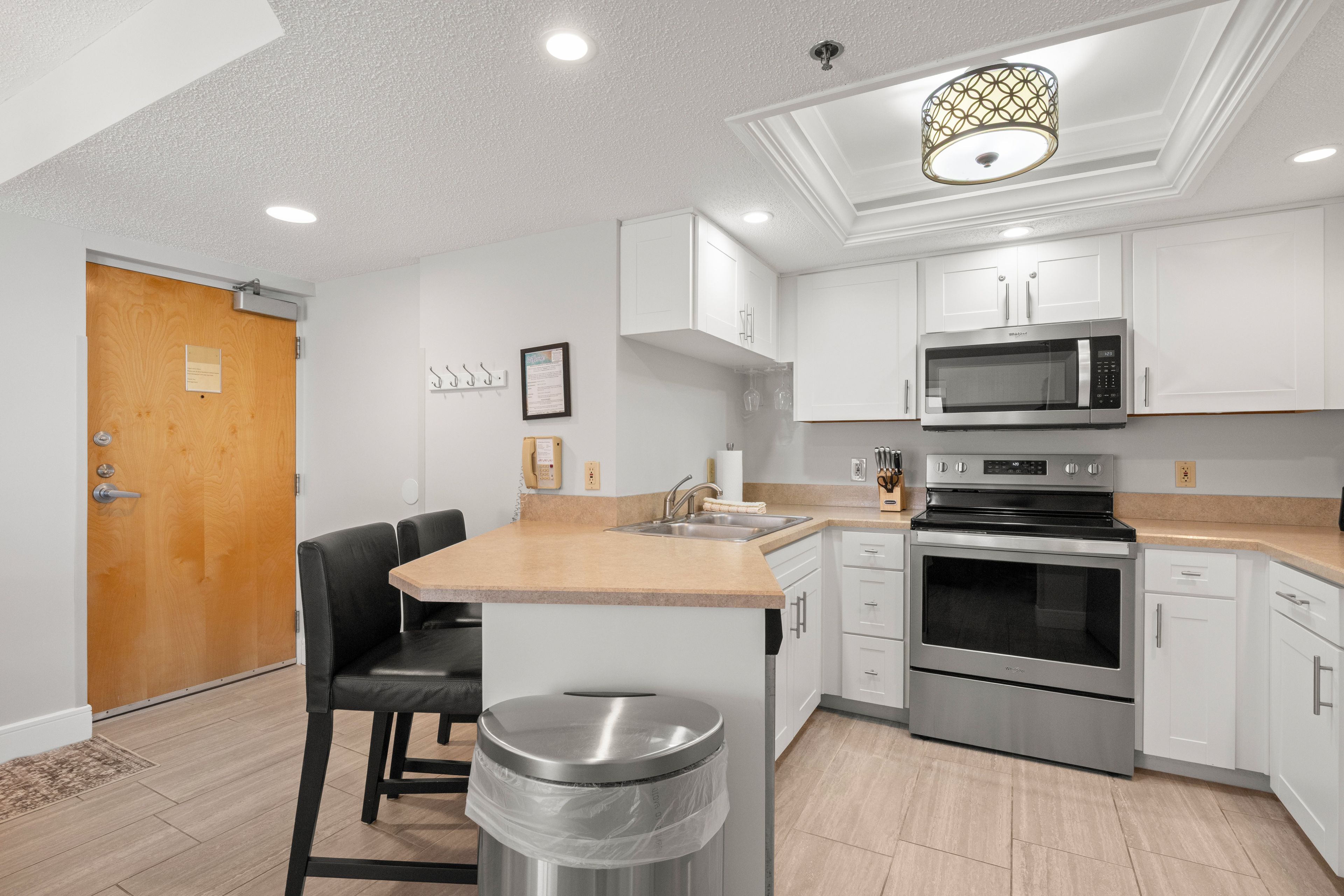 A modern kitchen with white cabinetry, stainless steel appliances, a wooden door, and a bar stool.