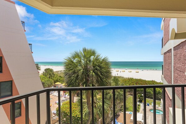 A balcony with a view of a beach, palm trees, and a pool.