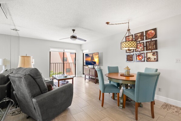 A modern living room with a grey sofa, a dining table with chairs, a ceiling fan, and artwork on the walls.
