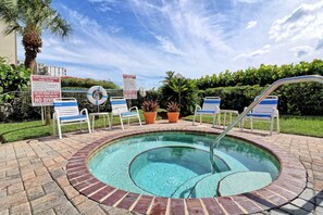 A pool area with lounge chairs and a hot tub, surrounded by palm trees and a clear sky.