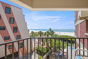 Un balcon avec vue sur une plage, des palmiers et un espace piscine.