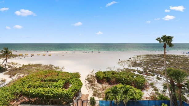 A beach with a clear sky, palm trees, and a sandy shore. - Gulf Front Condo with Panoramic Views of the Gulf (St Pete Beach)