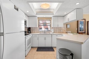 A modern kitchen with white cabinetry, a built-in oven, a microwave, a coffee maker, and a sink.
