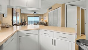 A kitchen with white cabinets, a beige countertop, and a ceiling fan. - Gulf Front Condo with Panoramic Views of the Gulf (St Pete Beach)