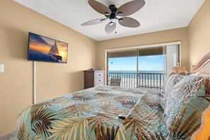 A bedroom with a bed, a ceiling fan, a TV, a dresser, a chair, and a balcony with a view.