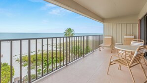 A balcony with a view of the beach, a table with chairs, and a railing. - Gulf Front Condo with Panoramic Views of the Gulf (St Pete Beach)