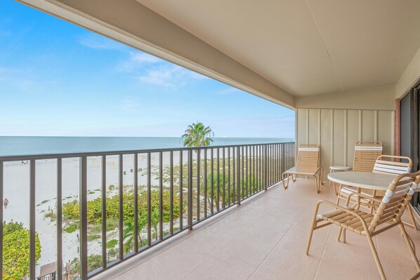 A balcony with a view of the beach, a table with chairs, and a railing.