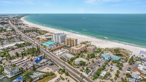 An aerial view of a coastal city with a beach, buildings, and a road.