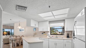 A modern kitchen with white cabinets, a large island, and a view of the beach through a window.