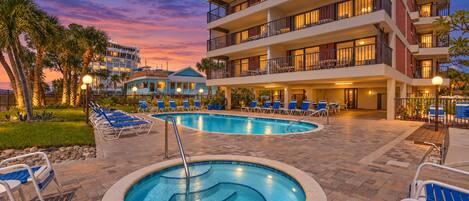 Un hotel con piscina, sillas de descanso y vistas al atardecer.