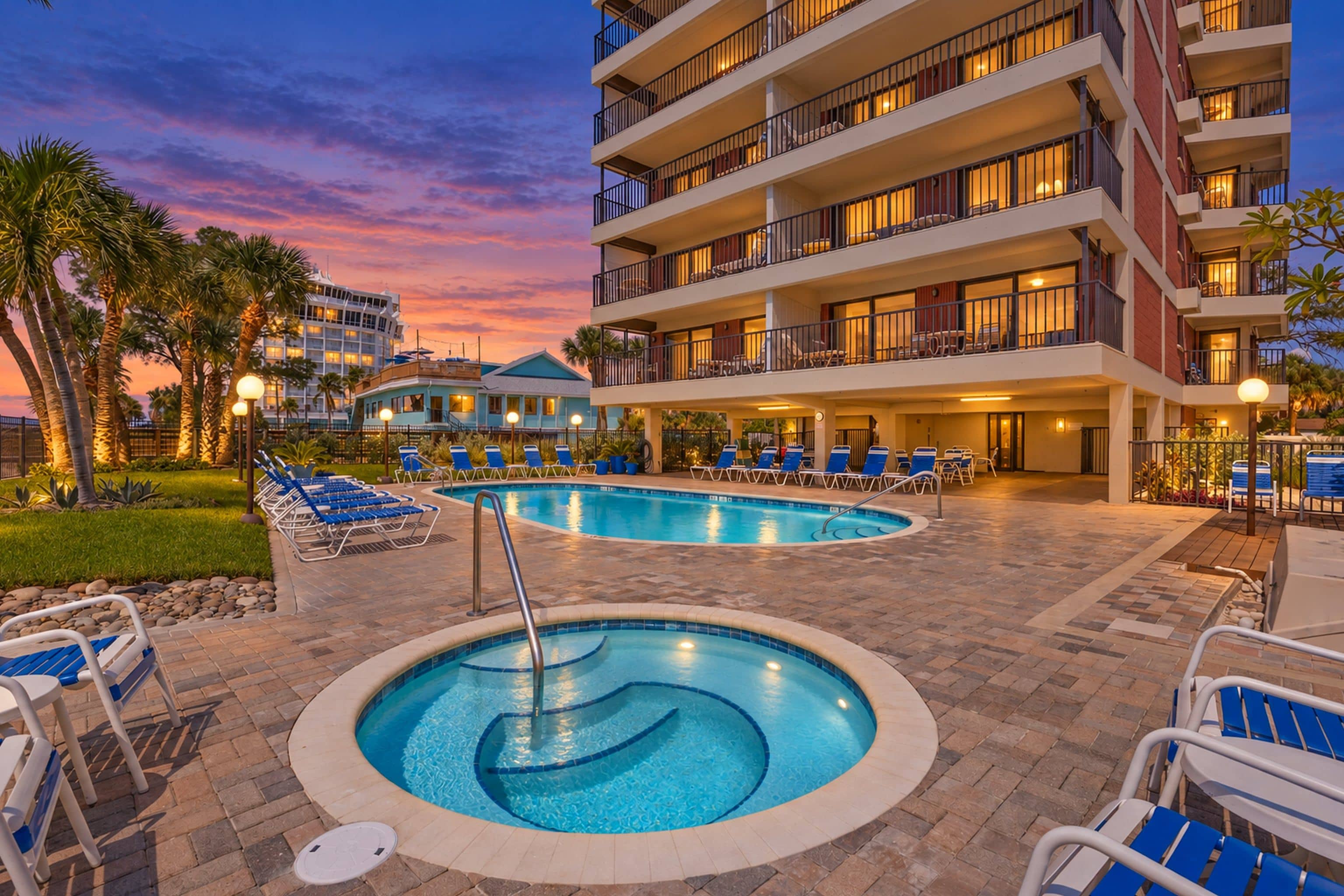 A hotel with a swimming pool, lounge chairs, and a sunset view.