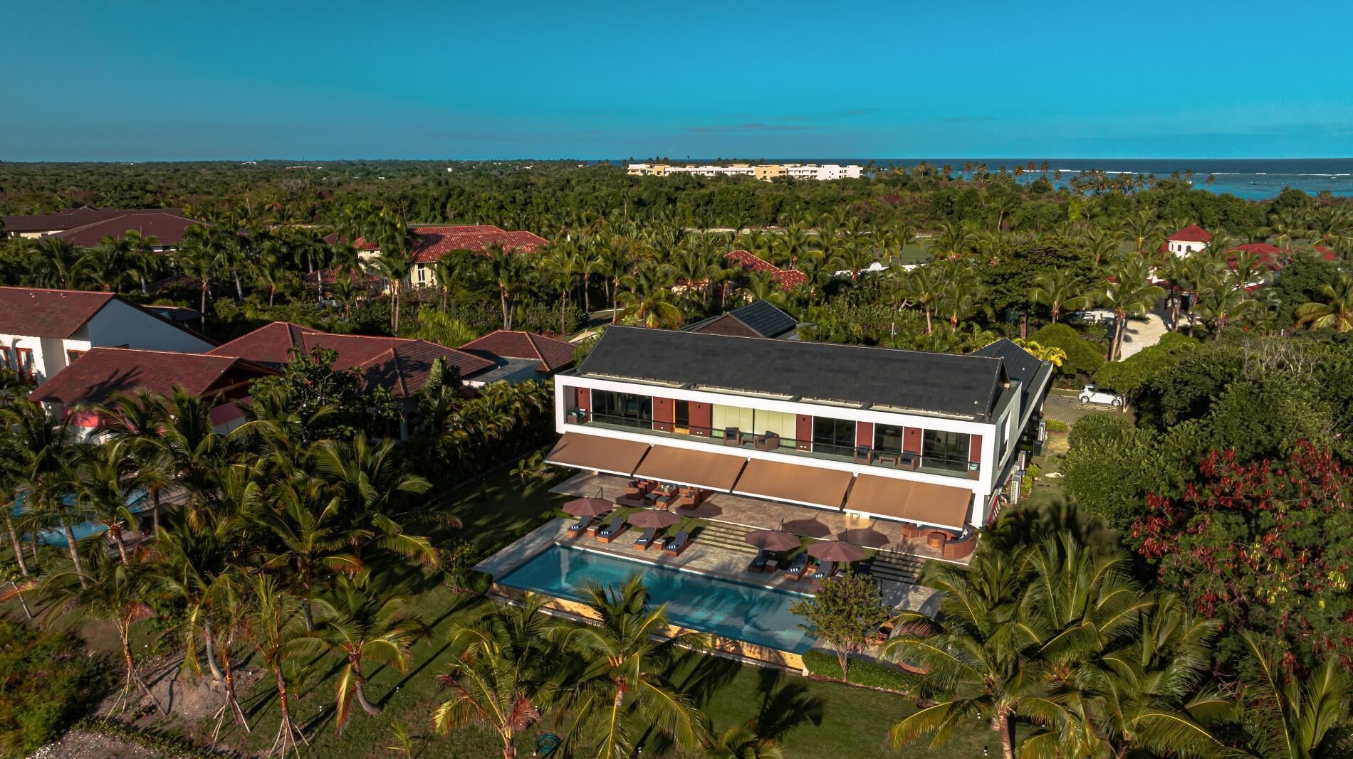 Un hôtel moderne doté d’une piscine, entouré de palmiers et offrant une vue sur l’océan.