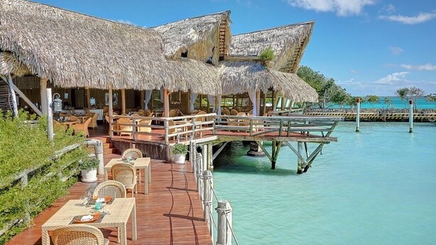 An overwater bungalows with thatched roofs, wooden deck, and dining area overlooking turquoise waters. - Large modern 7BDR villa with service staff with pool, close to beach and golf (Punta Cana)