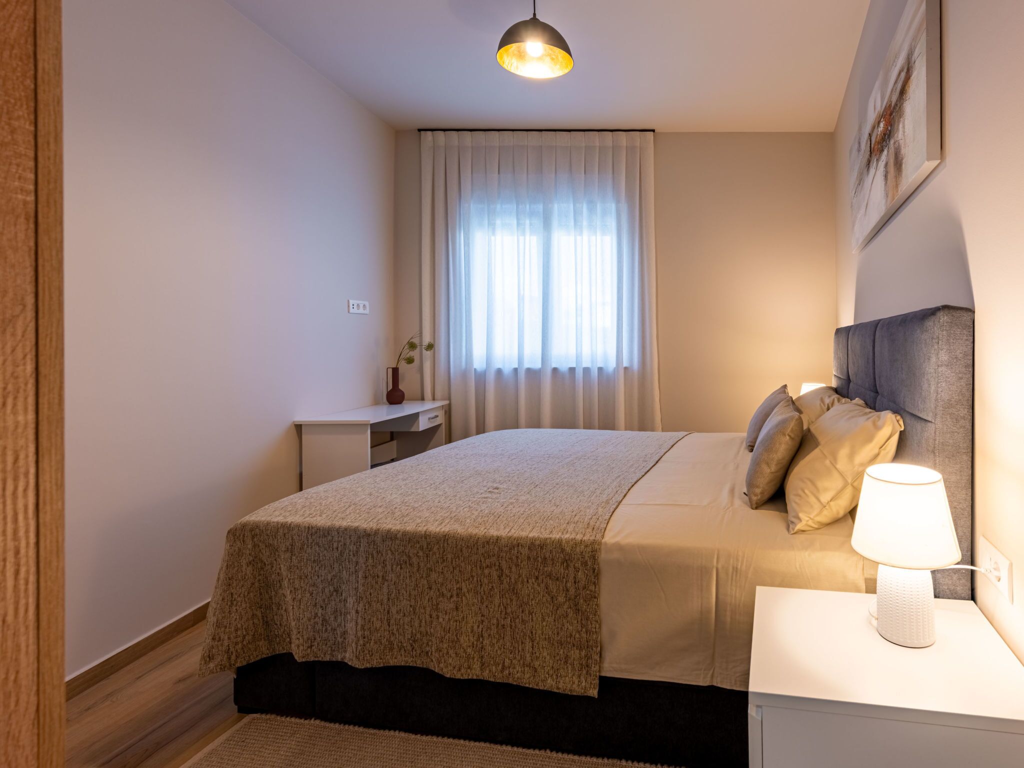 A bedroom with a bed, bedside table, lamp, and a window with curtains.