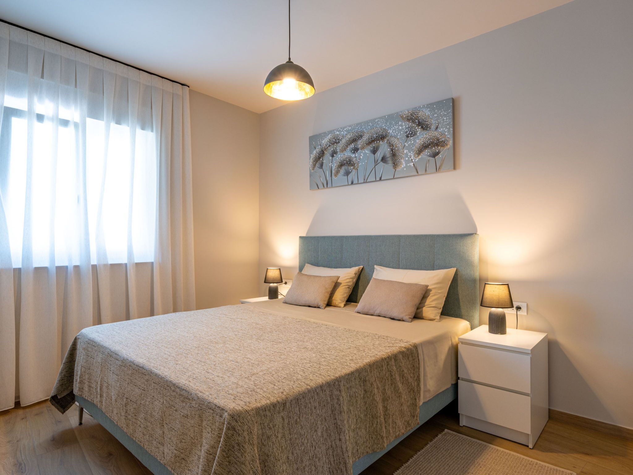 Ein Schlafzimmer mit einem großen Bett, zwei Nachttischen, einer Pendelleuchte und einem Wandbild.