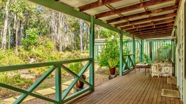 A covered wooden deck with a metal roof, surrounded by greenery and trees.