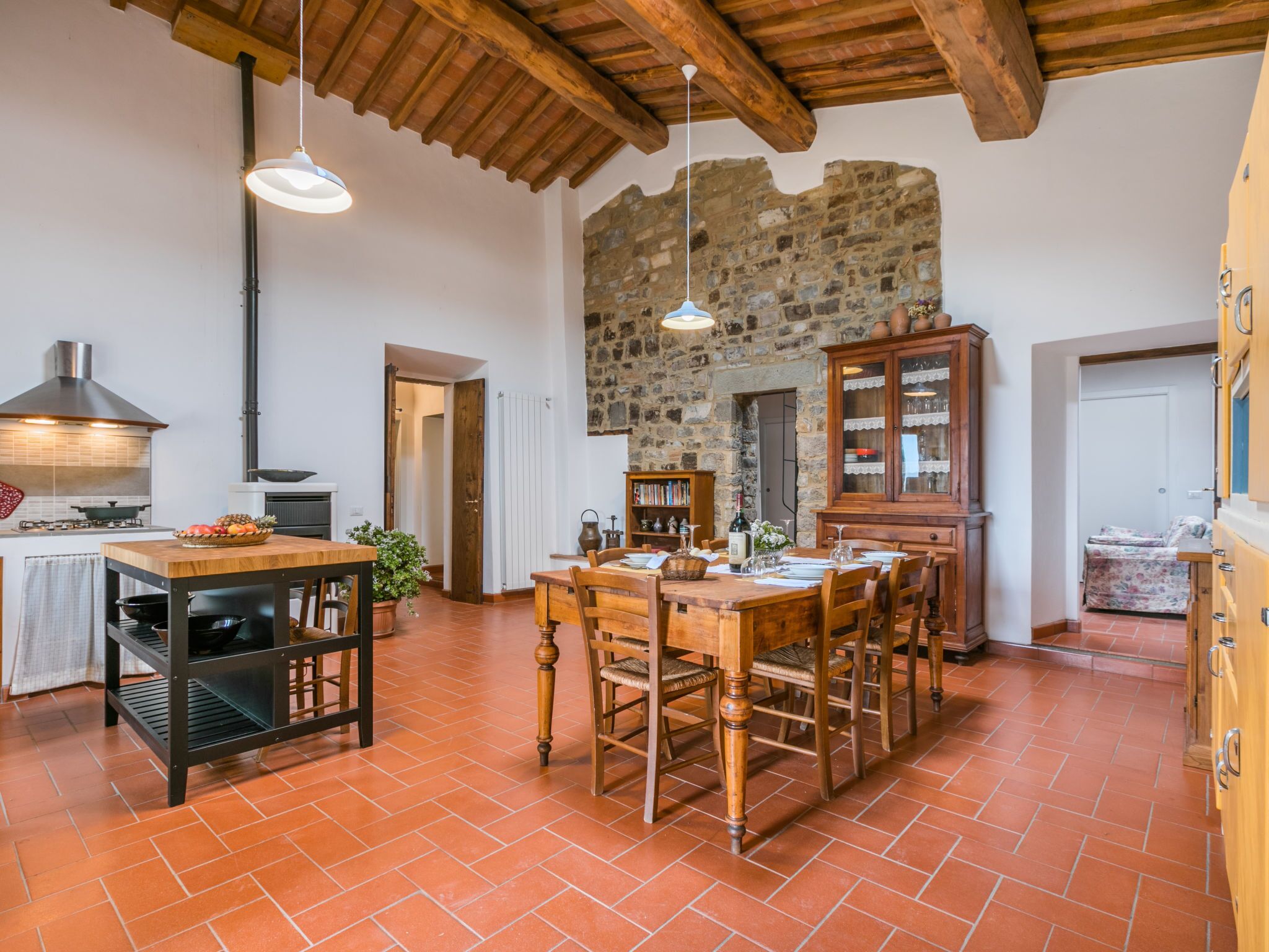 A rustic kitchen with a stone wall, wooden ceiling beams, and terracotta tiles.