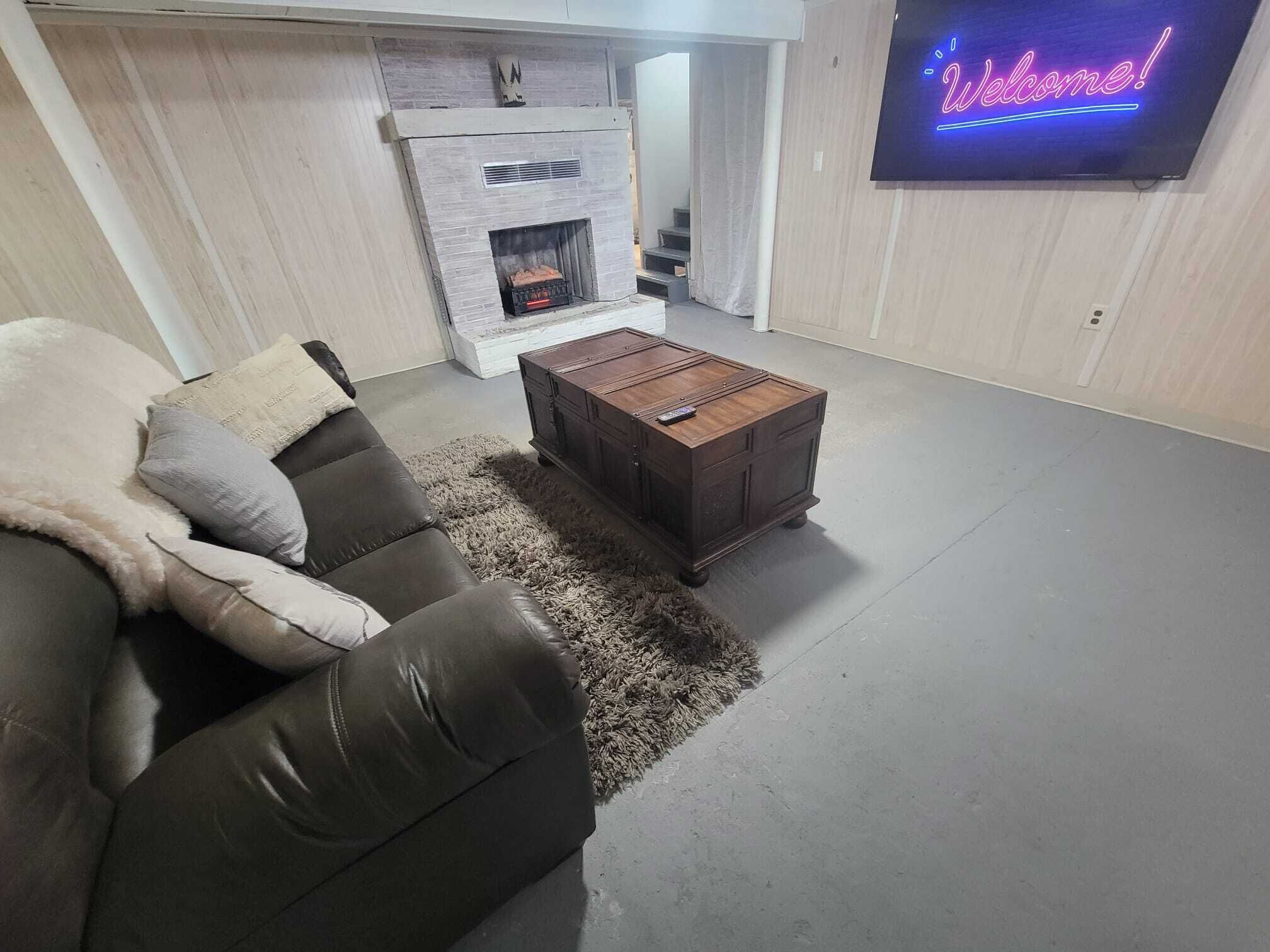 Una sala de estar con un sofá de cuero, una mesa de centro de madera, una chimenea y un televisor montado en la pared.