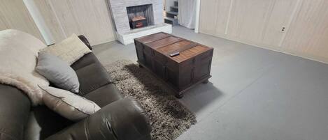 Una sala de estar con un sofá de cuero, una mesa de centro de madera, una chimenea y un televisor montado en la pared.