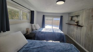 Et soveværelse med to senge, et vindue, en loftlampe og en trævæg med hylder.