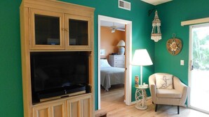 A living room with a large TV, wooden cabinets, a chair, and a small table.