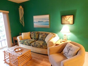 A living room with a green wall, a sofa, a chair, a lamp, and a wooden crate. - Beachwalk 2/2 Ground floor, handicap accessible (Fort Myers)