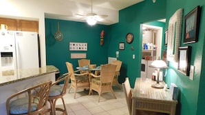 A kitchen with teal walls, a dining area with wicker chairs, a refrigerator, and a ceiling fan.