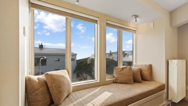 A room with a large window seat, a white radiator, and a view of buildings outside. - Central Chalet Hotham 11 (Hotham Heights)