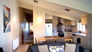 A modern living room with a sofa and a dining table, connected to a kitchen with a stove and a sink. - Central Chalet Hotham 11 (Hotham Heights)