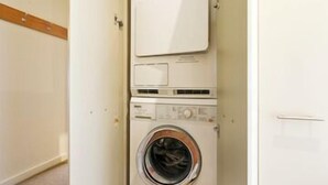 A compact, white laundry room with a front-loading washer and dryer. - Central Chalet Hotham 11 (Hotham Heights)