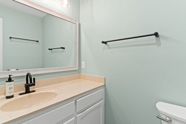 A bathroom with a beige sink, a black faucet, a large mirror, and a black towel rack.