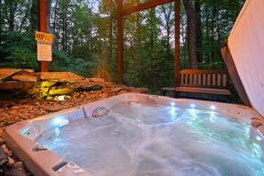 Ein Whirlpool in einer bewaldeten Gegend mit einer Holzterrasse und einem Schild, das vor Steinen und Felsen warnt.