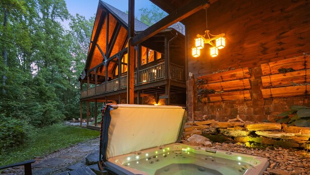 A hot tub with a control panel, surrounded by wooden decking and a stone wall.