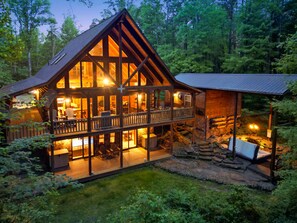 A log cabin with a balcony, surrounded by a forest.