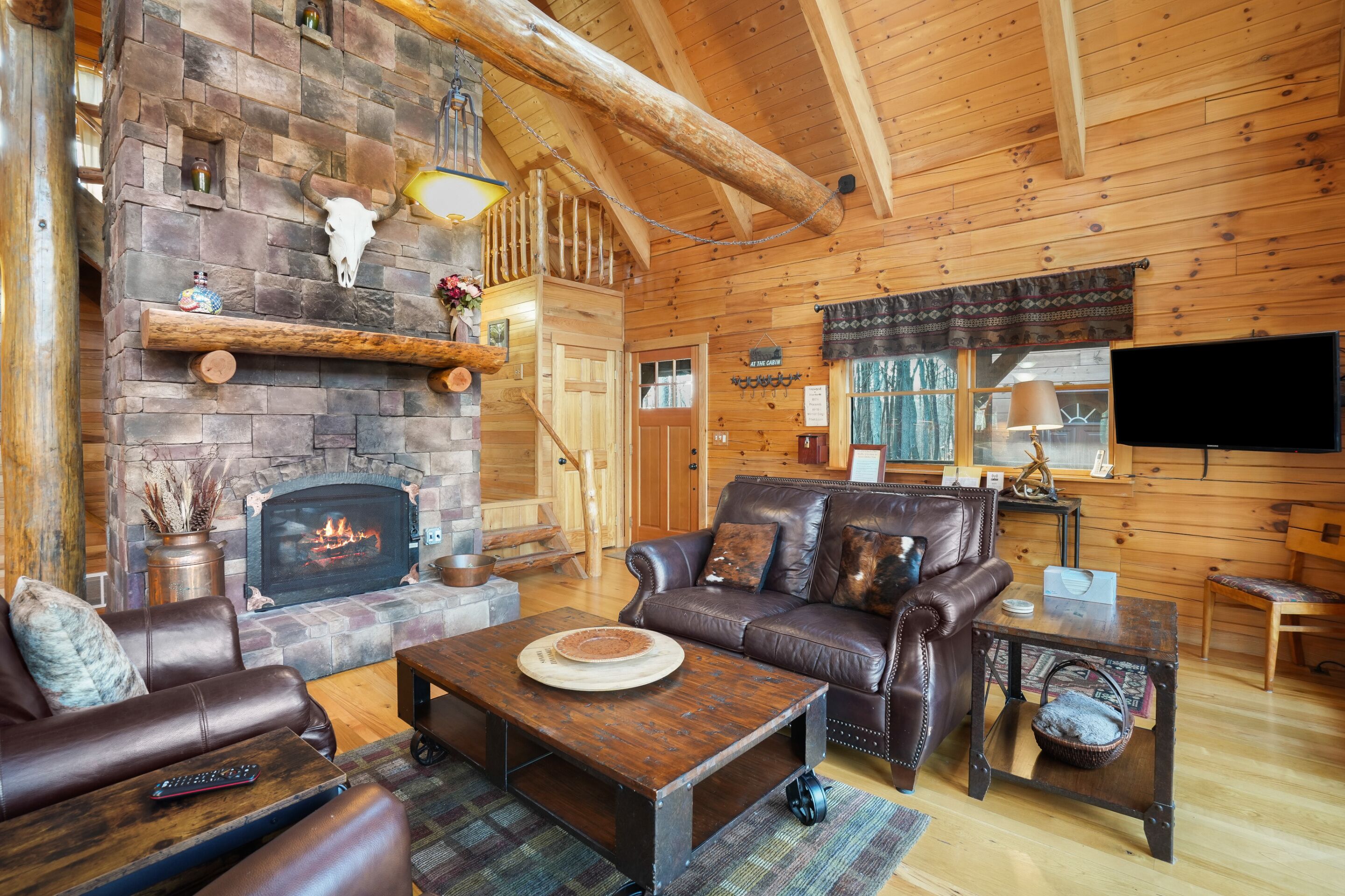 A cozy cabin interior with a stone fireplace, leather furniture, and a television.