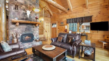 Un interior de cabaña acogedor con chimenea de piedra, muebles de cuero y un televisor.