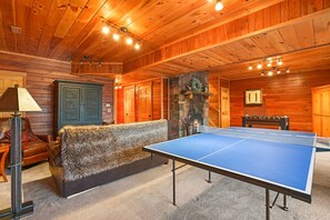 Ein Zimmer mit einem Tischtennisschrank, einer mit Fell bezogenen Couch, Holzwänden und einem Steinkamin.