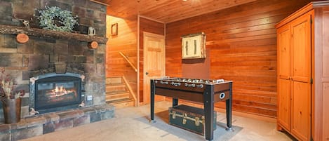 A cozy room with a stone fireplace, wooden walls, a foosball table, and a door leading to another area.