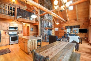 L’intérieur d’un chalet rustique est agrémenté d’une cheminée en pierre, d’une table à manger en bois et d’une cuisine équipée d’une cuisinière et d’un four.
