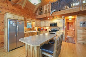 A log cabin interior with a kitchen featuring a stainless steel refrigerator, wooden cabinets, a microwave, and a large island with seating.
