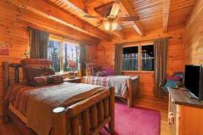 Ein Schlafzimmer einer Holzhütte mit zwei Betten, einem Deckenventilator und einem Fernseher.