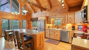 A wooden cabin interior with a large dining table, kitchen area, and built-in cabinets.