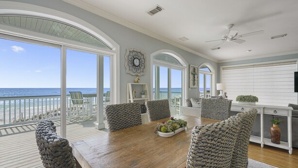 A spacious dining area with a wooden table, multiple chairs, and a view of the ocean.