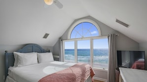 A bedroom with a large bed, a TV, and a view of the ocean.