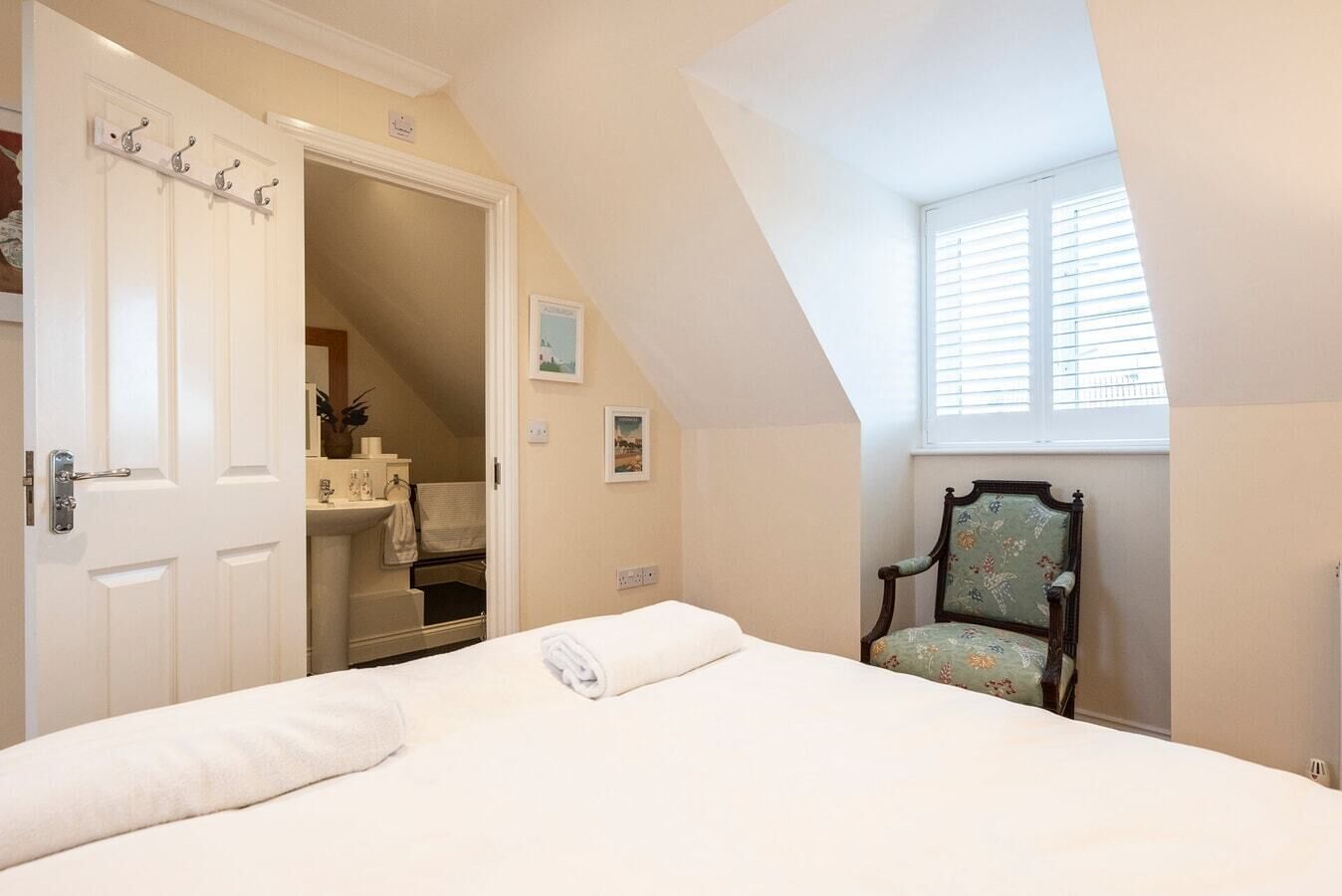 Une chambre à coucher avec un lit, une chaise, une salle de bain avec un lavabo et une fenêtre avec des stores.