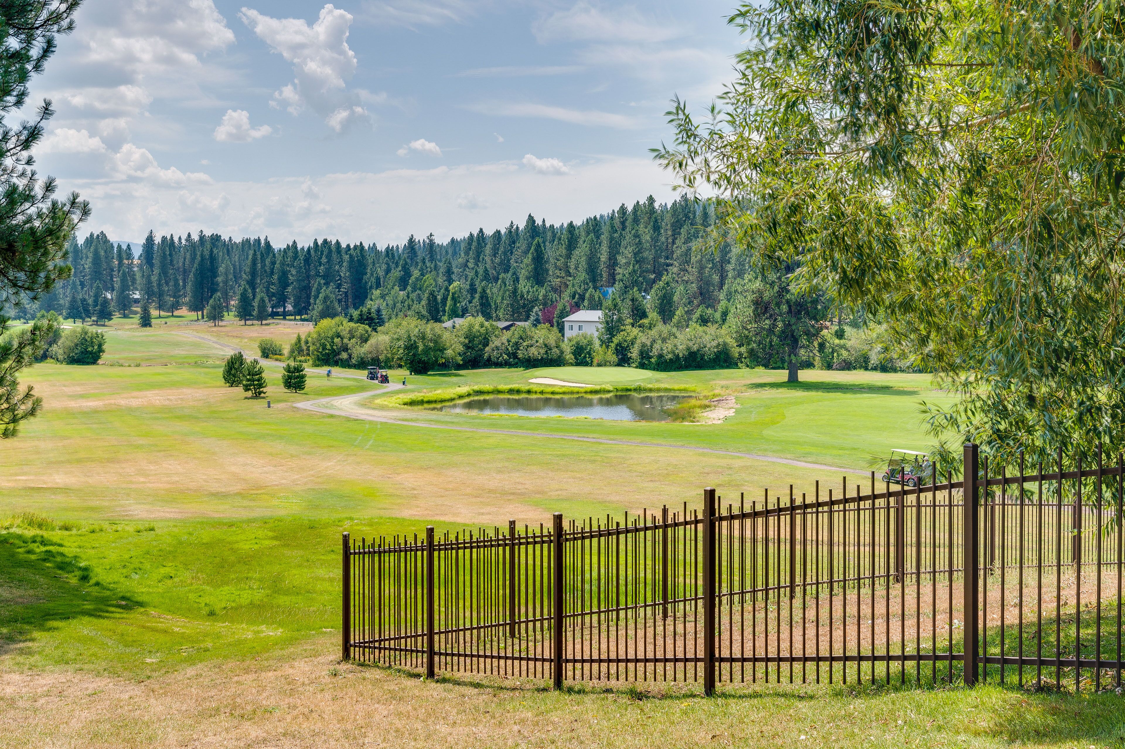 Un parcours de golf avec un étang, entouré d’arbres et d’une clôture.
