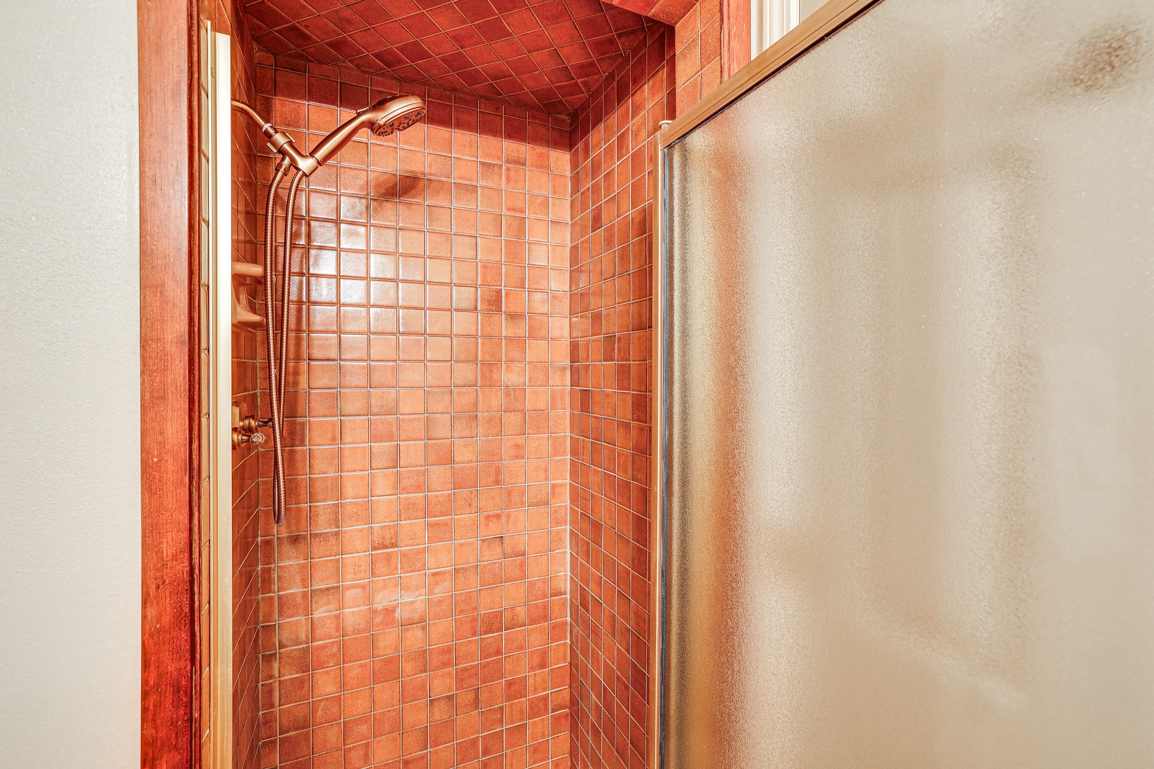 A shower with a tiled wall and a wooden door frame.
