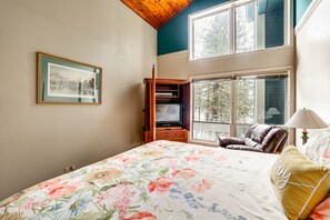 Une chambre à coucher avec un grand lit, une armoire en bois, une télévision et une fenêtre donnant sur les arbres.