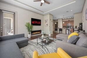 A modern living room with a fireplace, grey sofas, a coffee table, and a kitchen in the background.
