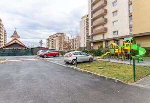 Un parcheggio con auto, un'area giochi con uno scivolo e edifici residenziali sullo sfondo.